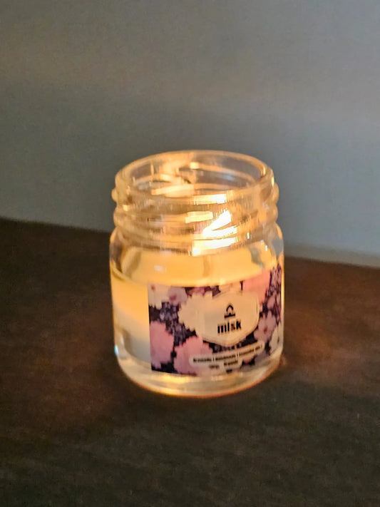 Illuminated candle in a glass jar with a floral label on a dark surface.