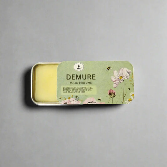 Solid perfume bar in a tin with 'Demure' packaging on a gray background