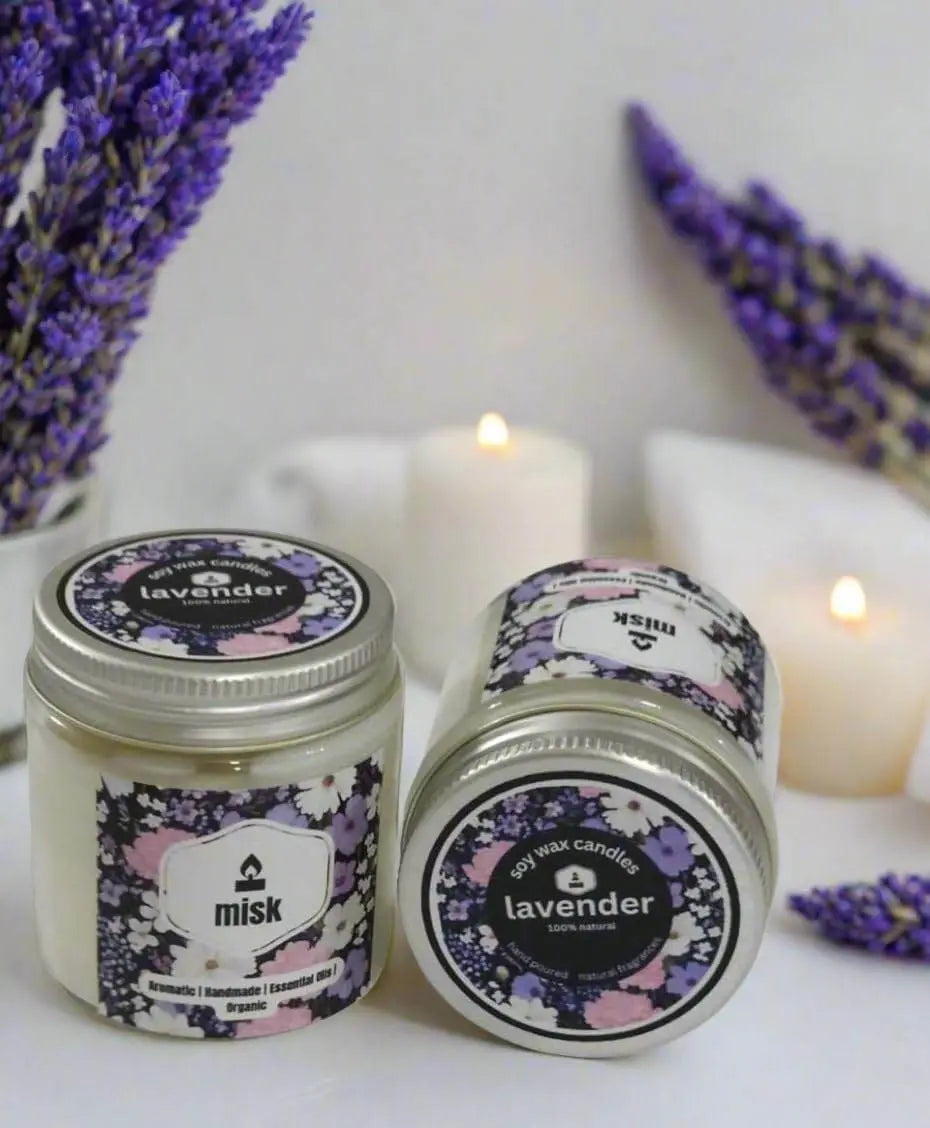 Two lavender-scented candles with decorative labels on a white surface with lavender flowers.