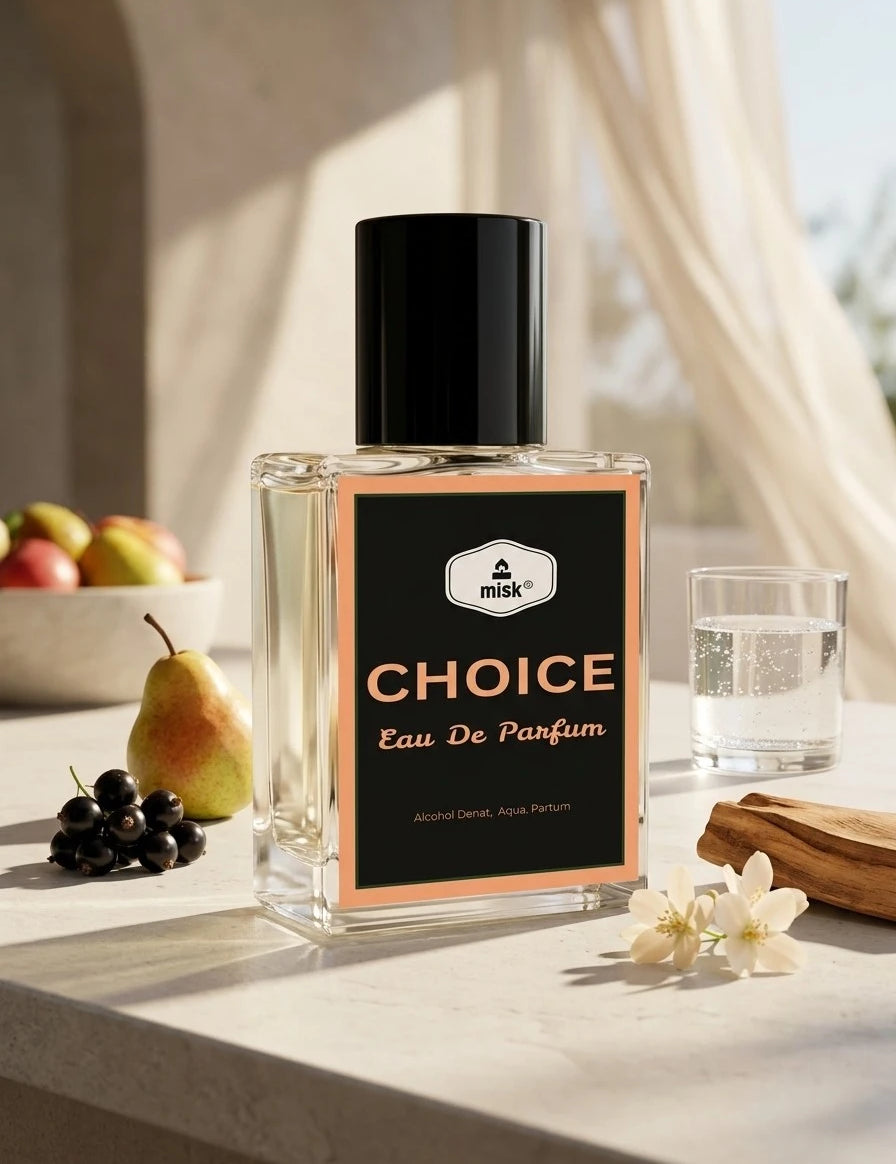 A clear rectangular perfume bottle labeled 'CHOICE Eau De Parfum' with a black cap and black label, styled on a light stone surface with fruit, a glass of water, and flowers in a bright indoor setting.