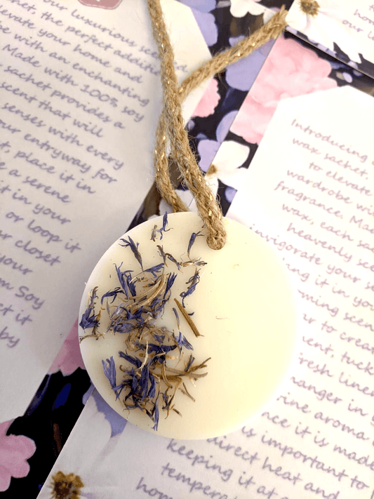 Round wax sachet with dried flowers on a string, placed on top of printed text.