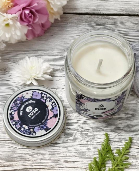On a white wooden table a Rose candle with the lid open with flowers strewn.