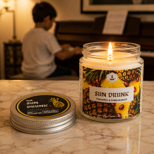 A burning Sun Drunk candle in the foreground on a marble top. A child playing a piano in the background